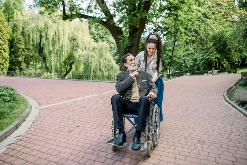 Homme en fauteuil roulant poussé par une jeune femme aux cheveux longs