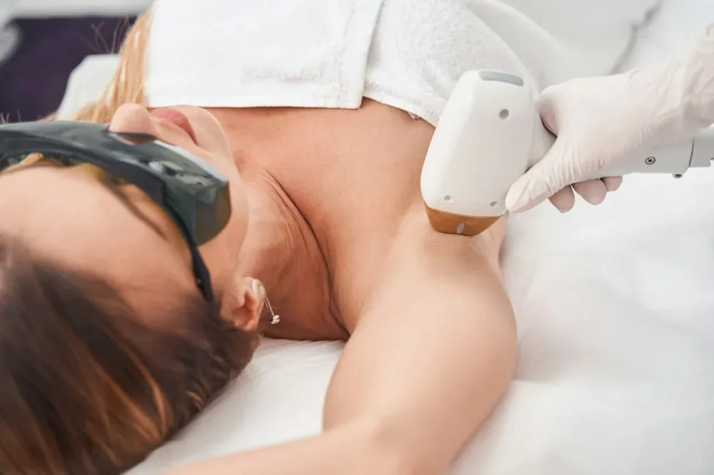 Épilation lumière pulsée : une professionnelle applique un appareil sur le bras d'une personne allongée.