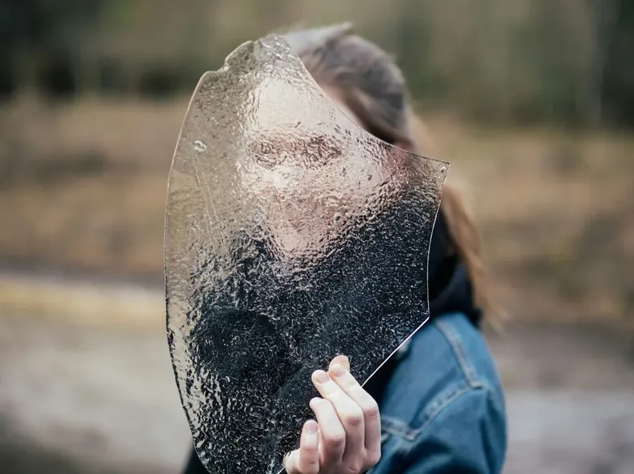 Une femme se tient derrière un verre dépoli pour illustrer métaphoriquement une difficulté de reconnaissance des visages