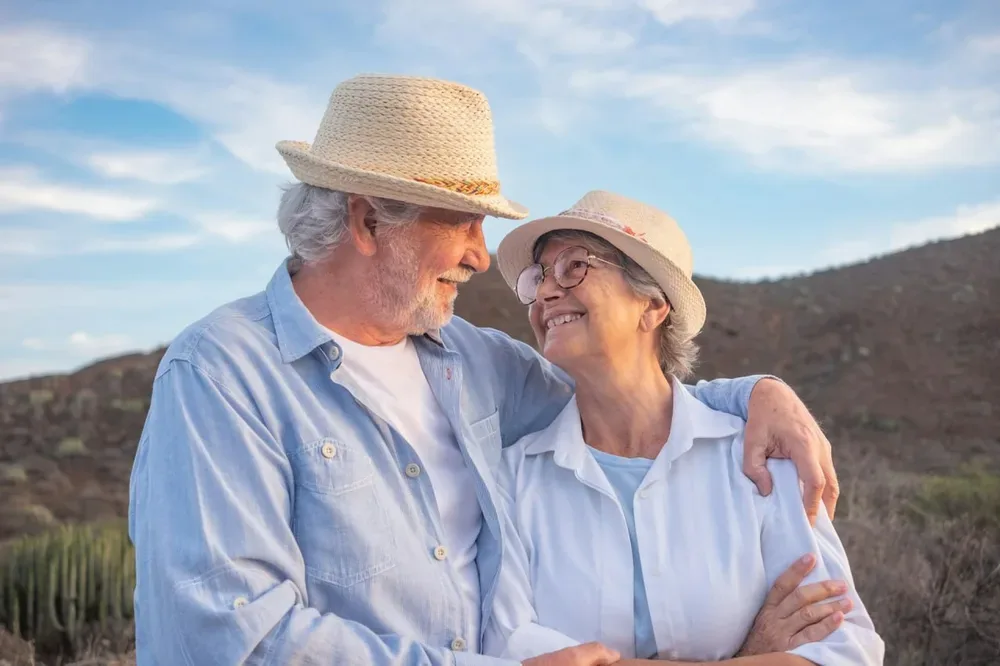 Senior : un couple souriant portant des chapeaux de paille dans un paysage en plein air