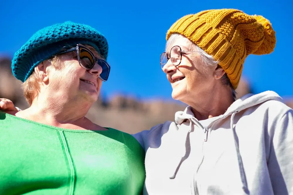 Senior : deux femmes souriantes portant des bonnets colorés lors d’une sortie en plein air